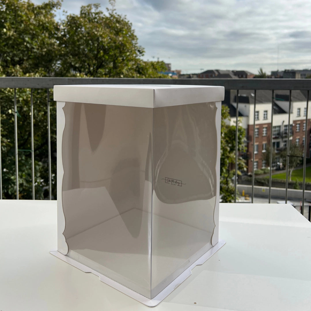 A clear crystal cake box with a 10 inch base and 14 inches tall, displayed on a balcony table.
