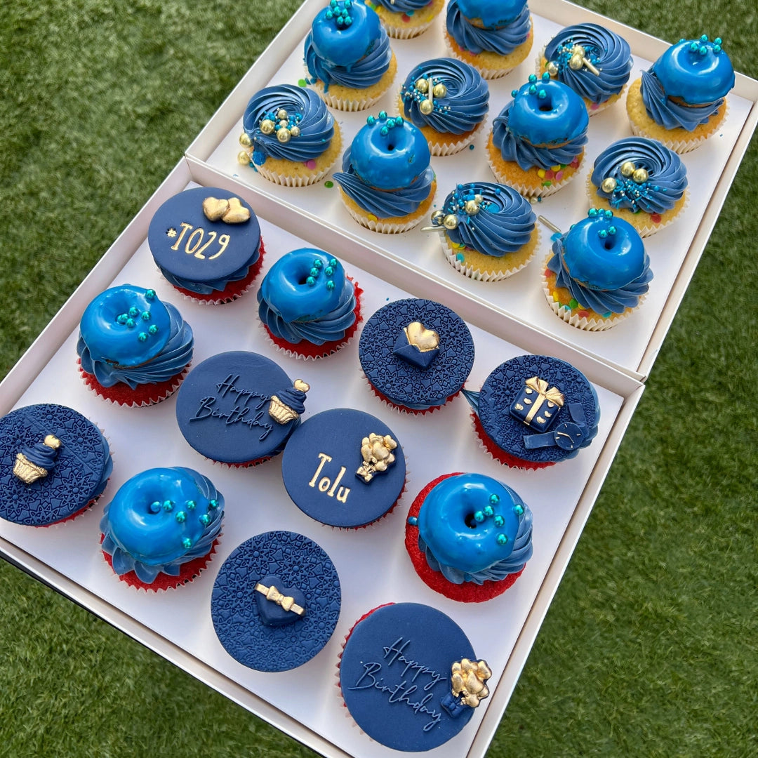 A TOP VIEW OF 24 BLUE FROSTED CUPCAKES DISPLAYED IN A FLAT WHITE CAKE BOX TRAY